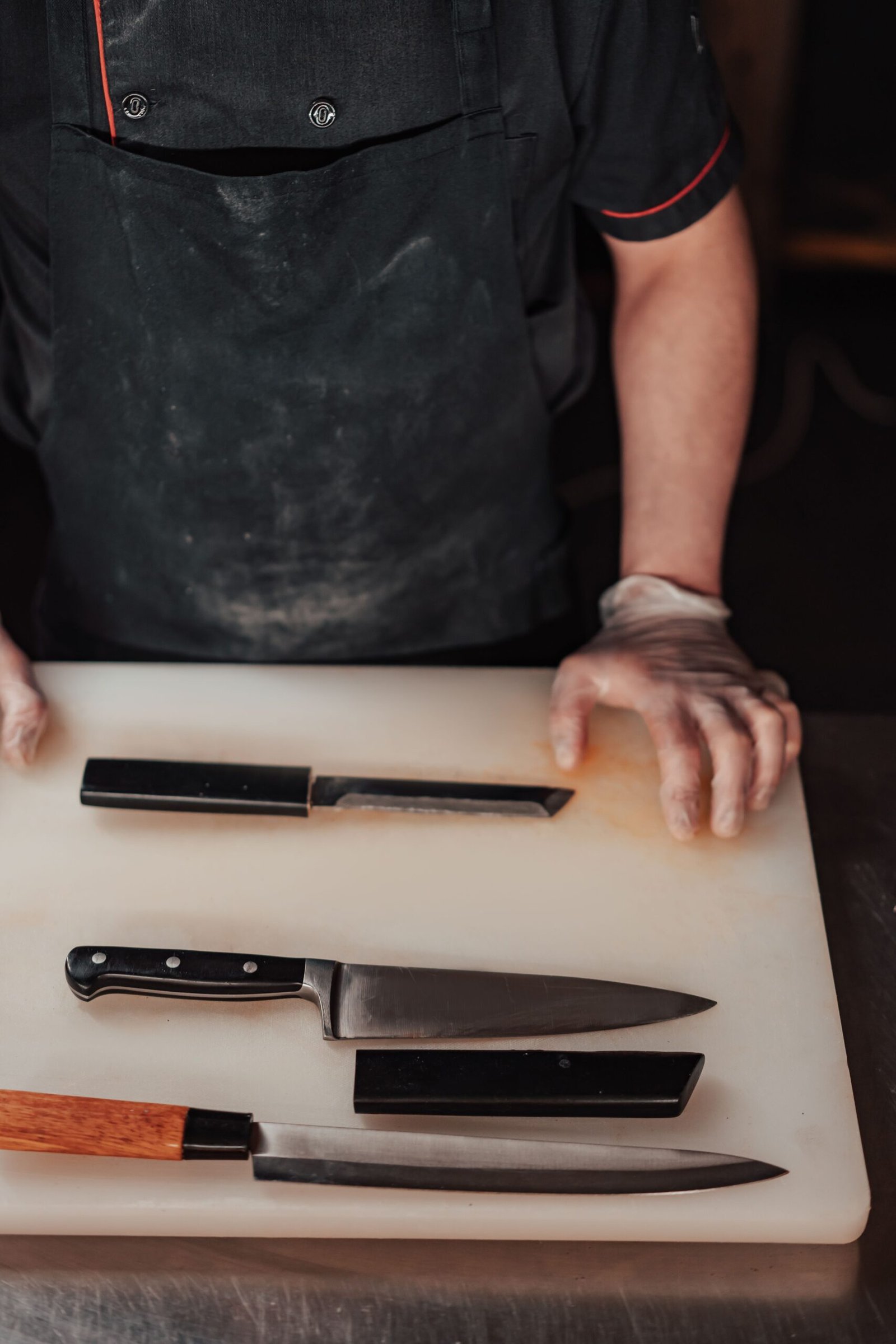 Chef in black apron preparing food with Japanese knives on a cutting board.